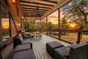 Ein überdachter Außenbereich mit Holzmöbeln und Blick auf Bäume und Sonnenuntergang.