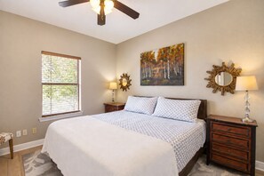 A bedroom with a large bed, two bedside tables, a ceiling fan, a window with blinds, and a painting on the wall. - Stargazers' dream home on 1.5 acres w/ telescope-near wineries-Dogs ok (Dripping Springs)