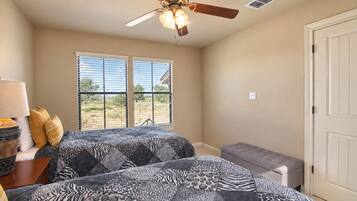 A bedroom with two beds, a ceiling fan, a window with blinds, and a door.