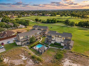 A residential area with multiple houses, a swimming pool, and a golf course in the background.