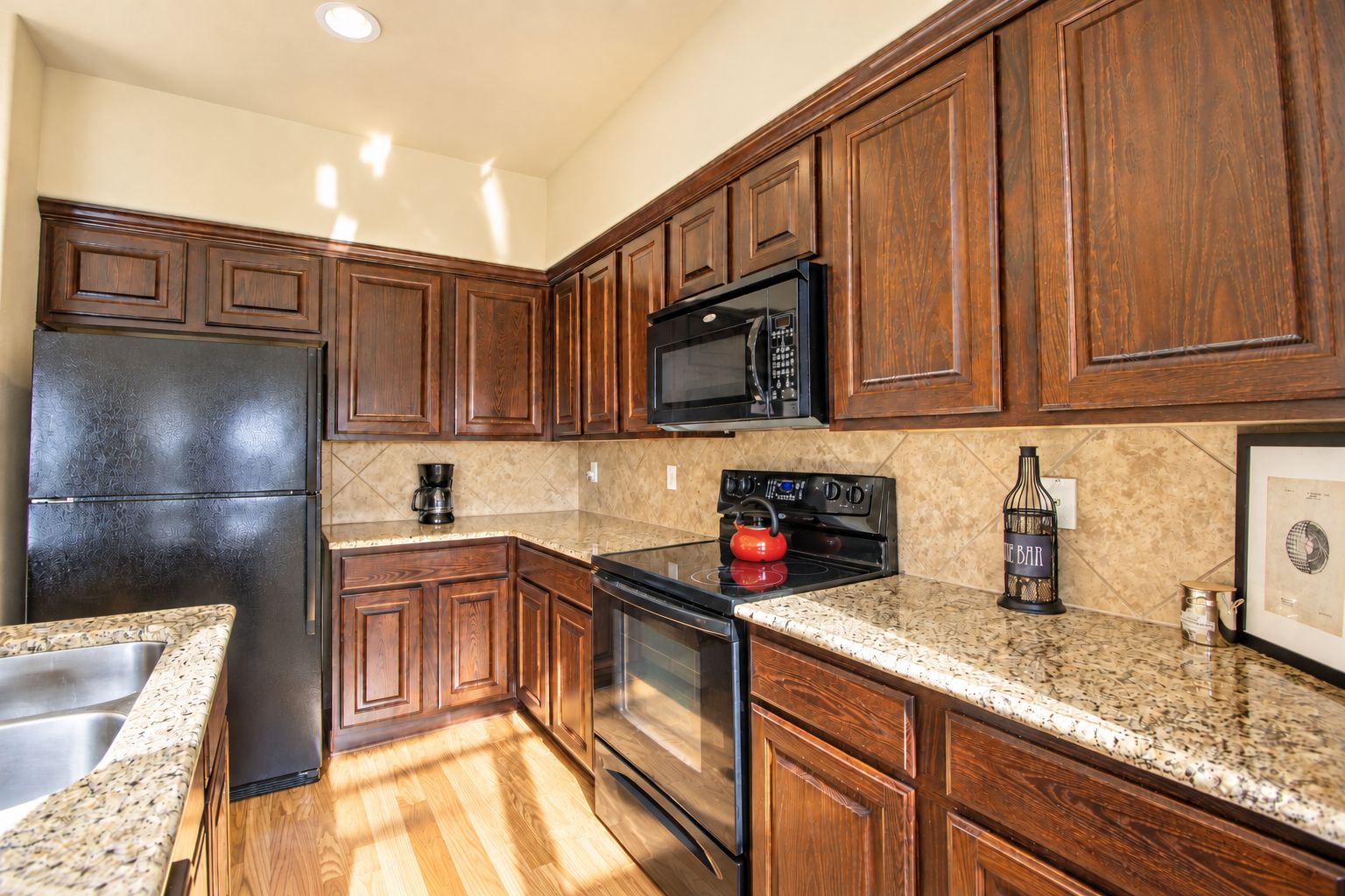 A kitchen with wooden cabinets, a stainless steel refrigerator, a microwave, a stove, and a coffee maker.