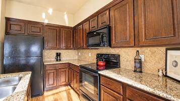 A kitchen with wooden cabinets, a stainless steel refrigerator, a microwave, a stove, and a coffee maker.