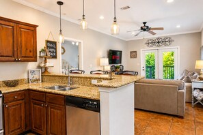 Une cuisine dotée de meubles en bois, d’un lave-vaisselle, de plans de travail en granit, de luminaires suspendus, d’un ventilateur de plafond et offrant une vue sur l’extérieur grâce à une porte vitrée.