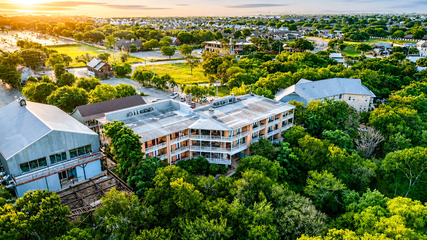 A multi-story building with balconies, surrounded by dense greenery and a clear sky.