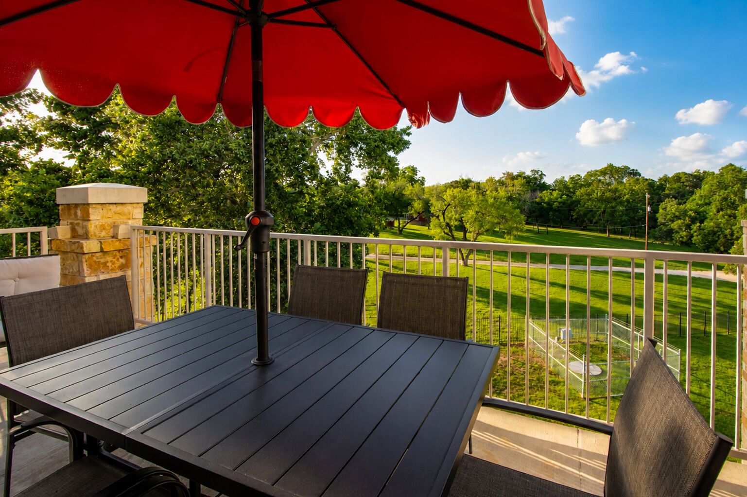 A deck with a table and chairs, a red umbrella, and a view of a golf course.