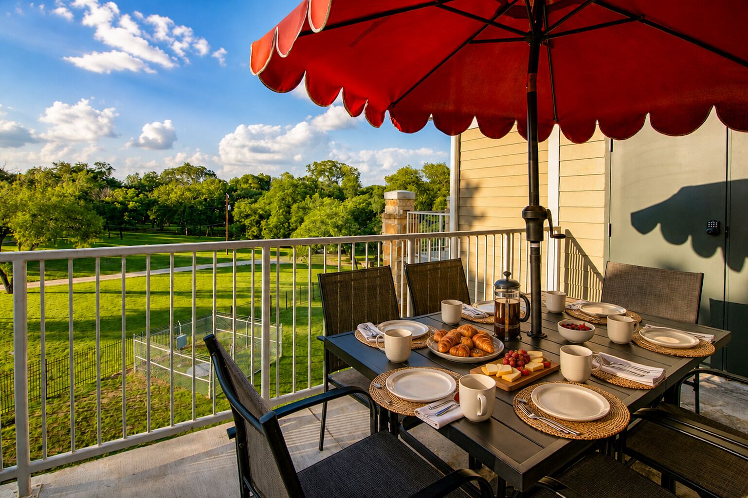 Un balcon avec une table préparée pour le petit-déjeuner, des sièges d’extérieur et une vue sur un paysage verdoyant.