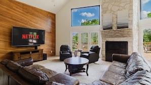A living room with a leather sofa, a coffee table, a fireplace, a stone wall, and a television displaying 'NETFLIX'. - Idyllic waterfront getaway with private hot tub & deck views - near golf (New Braunfels)