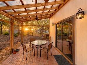 Un patio cubierto con una mesa redonda y sillas, una pérgola de madera y un amplio ventanal que da al exterior.