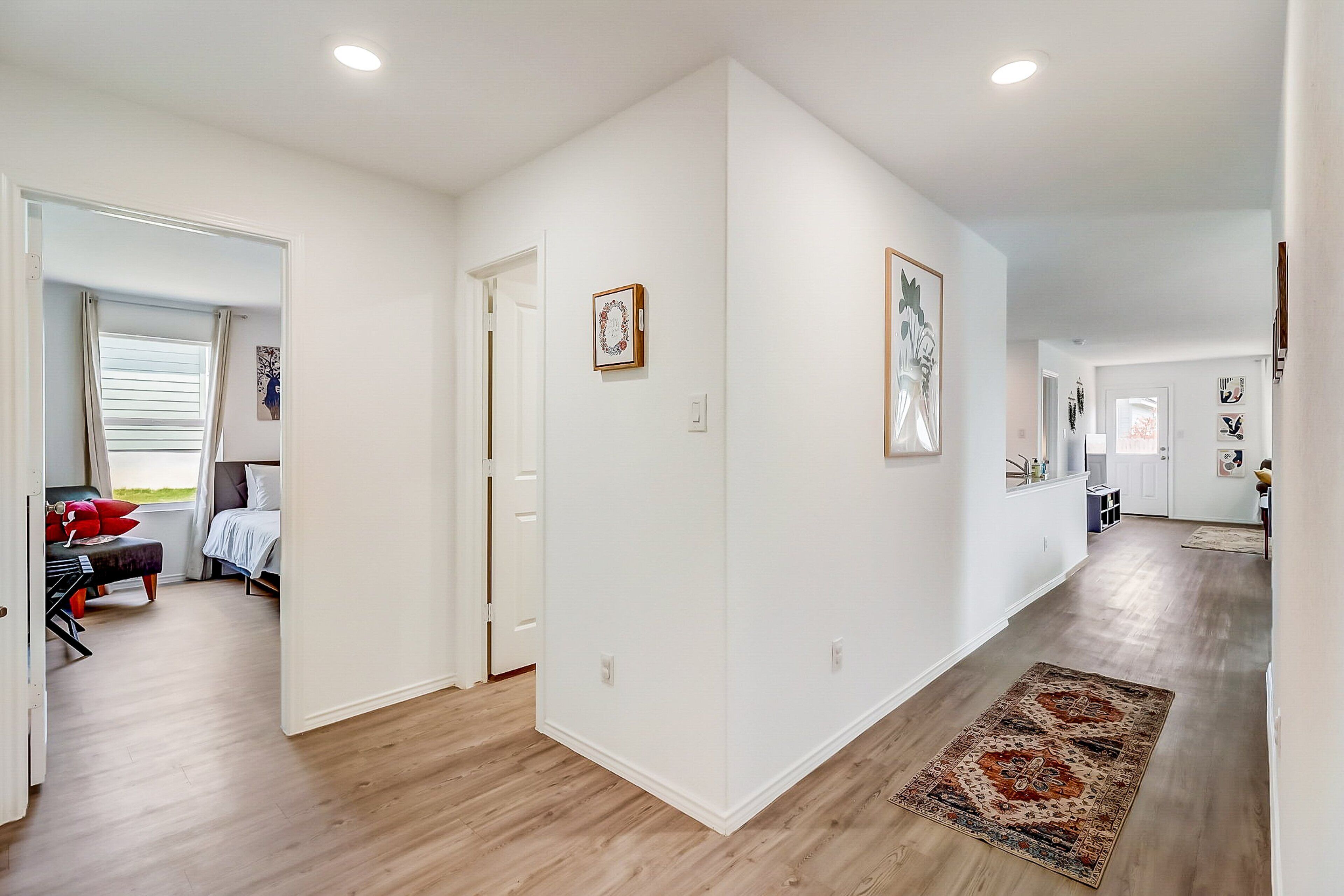 A hallway with wooden flooring, white walls, and a patterned rug.