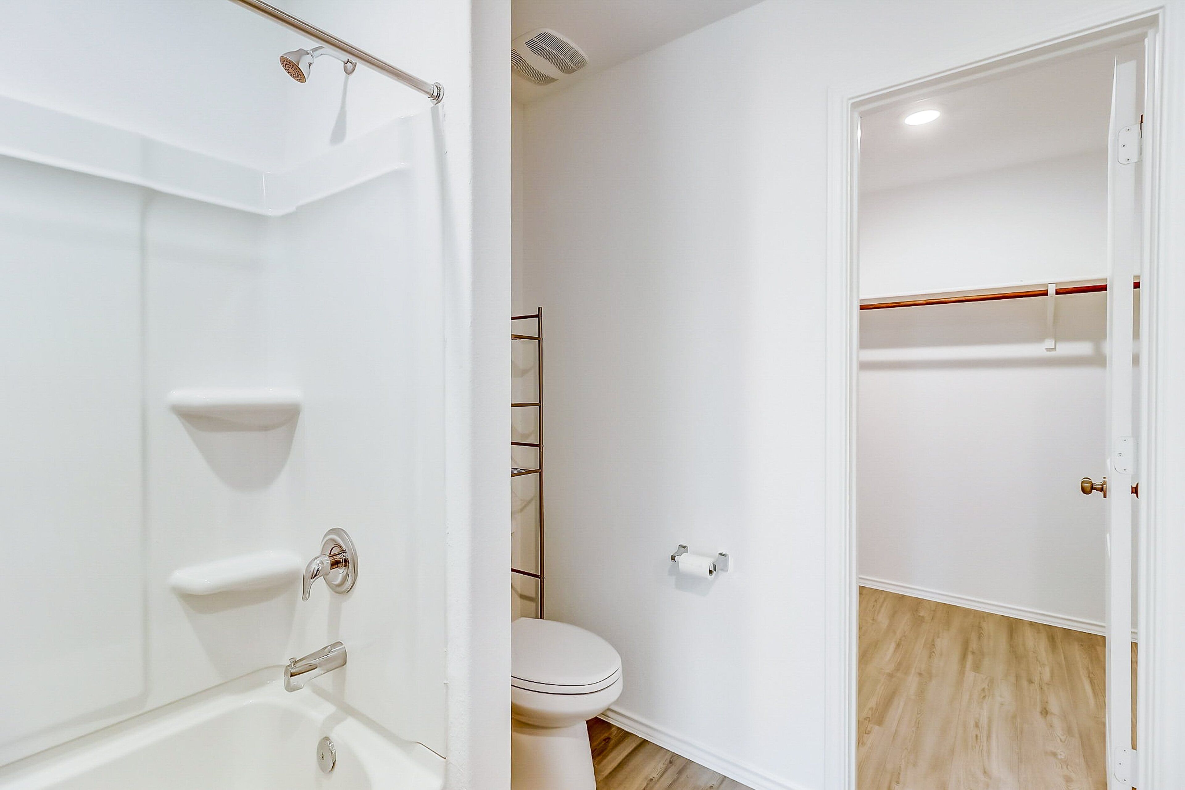 A bathroom with a bathtub, toilet, and a walk-in closet with a wooden floor.