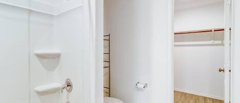 A bathroom with a bathtub, toilet, and a walk-in closet with a wooden floor.