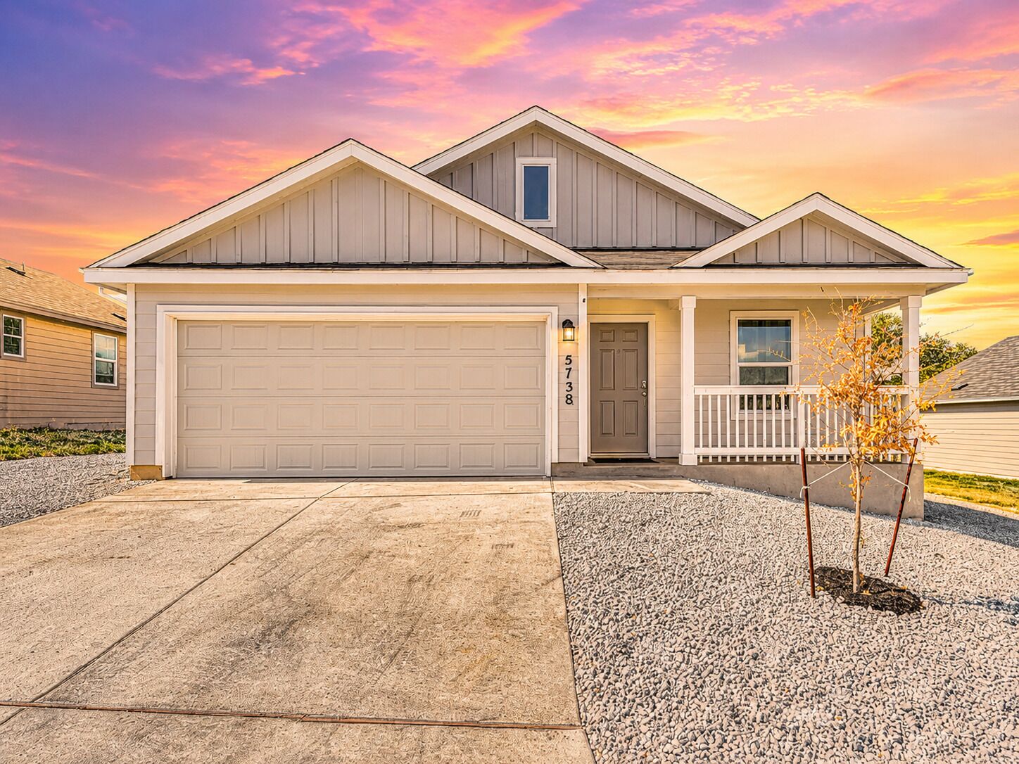 A two-story house with a garage, a front porch, and a small tree in the driveway.