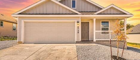 A two-story house with a garage, a front porch, and a small tree in the driveway.