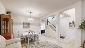 A spacious living room with a white sofa, a dining table with chairs, a patterned rug, and a staircase leading to another level. - 2-story house with back patio, grill, streaming, washer/dryer, & 2 living areas (San Antonio)