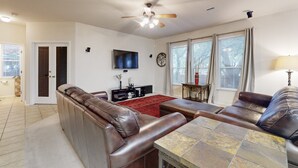 A spacious living room with leather sofas, a flat-screen TV, a ceiling fan, and a large window with curtains. - 2-story house with back patio, grill, streaming, washer/dryer, & 2 living areas (San Antonio)