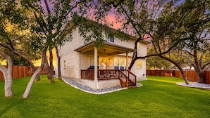 A two-story house with a covered porch, a front yard with a well-maintained lawn, and a wooden fence. - 2-story house with back patio, grill, streaming, washer/dryer, & 2 living areas (San Antonio)