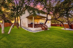 A two-story house with a covered porch, a front yard with a well-maintained lawn, and mature trees. - 2-story house with back patio, grill, streaming, washer/dryer, & 2 living areas (San Antonio)