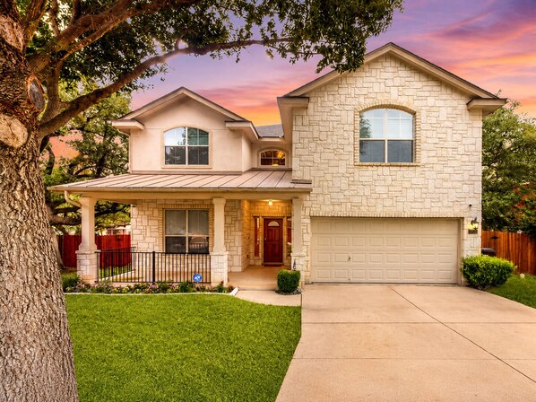 A two-story house with a stone facade, a covered porch, and a garage. - 2-story house with back patio, grill, streaming, washer/dryer, & 2 living areas (San Antonio)