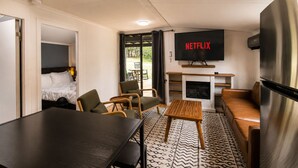Moderni hotellihuone, jossa on sänky, oleskelualue, televisio, takka ja ruokapöytä.