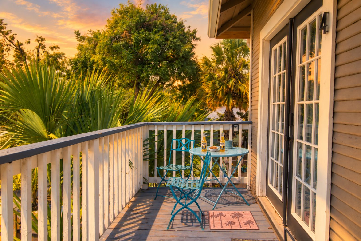 A wooden deck with a white railing, a round table with chairs, and a door to a building.