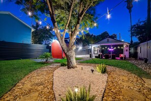 Ein Garten mit Baum, Lichterkette, kleiner Gartenhütte und einer Terrasse.