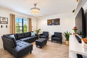A modern living room with a sectional sofa, two armchairs, a coffee table, a chandelier, a flat-screen TV, and a painting on the wall. - Picture Your Stay | Beautifully renovated home (San Antonio)