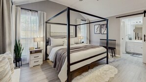 A four-poster bed with a wooden frame, a bedside table with a lamp, a chair, and a large mirror in a modern bedroom with light wooden flooring and a ceiling fan. - Stunning Rivrefront 3BR with Hot tub, water view! (Seguin)