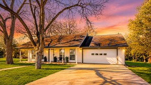 A single-story house with a covered porch, a garage, and a well-maintained lawn. - Stunning Rivrefront 3BR with Hot tub, water view! (Seguin)