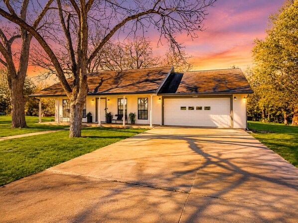A single-story house with a covered porch, a garage, and a well-maintained lawn. - Stunning Riverfront 3BR with Hot tub, water view! (Seguin)