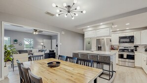 A modern kitchen with white cabinetry, a wooden dining table, and a central island. - Stunning Rivrefront 3BR with Hot tub, water view! (Seguin)