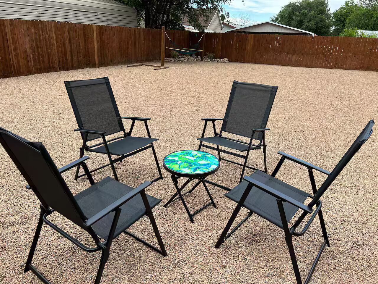 A patio area with four black metal chairs and a round table with a green and blue patterned tabletop.