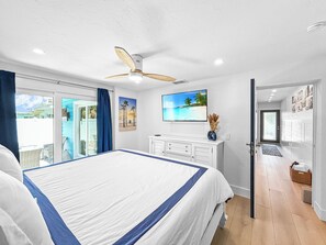 Ein Schlafzimmer mit Bett, Deckenventilator, Fernseher und Blick ins Freie.