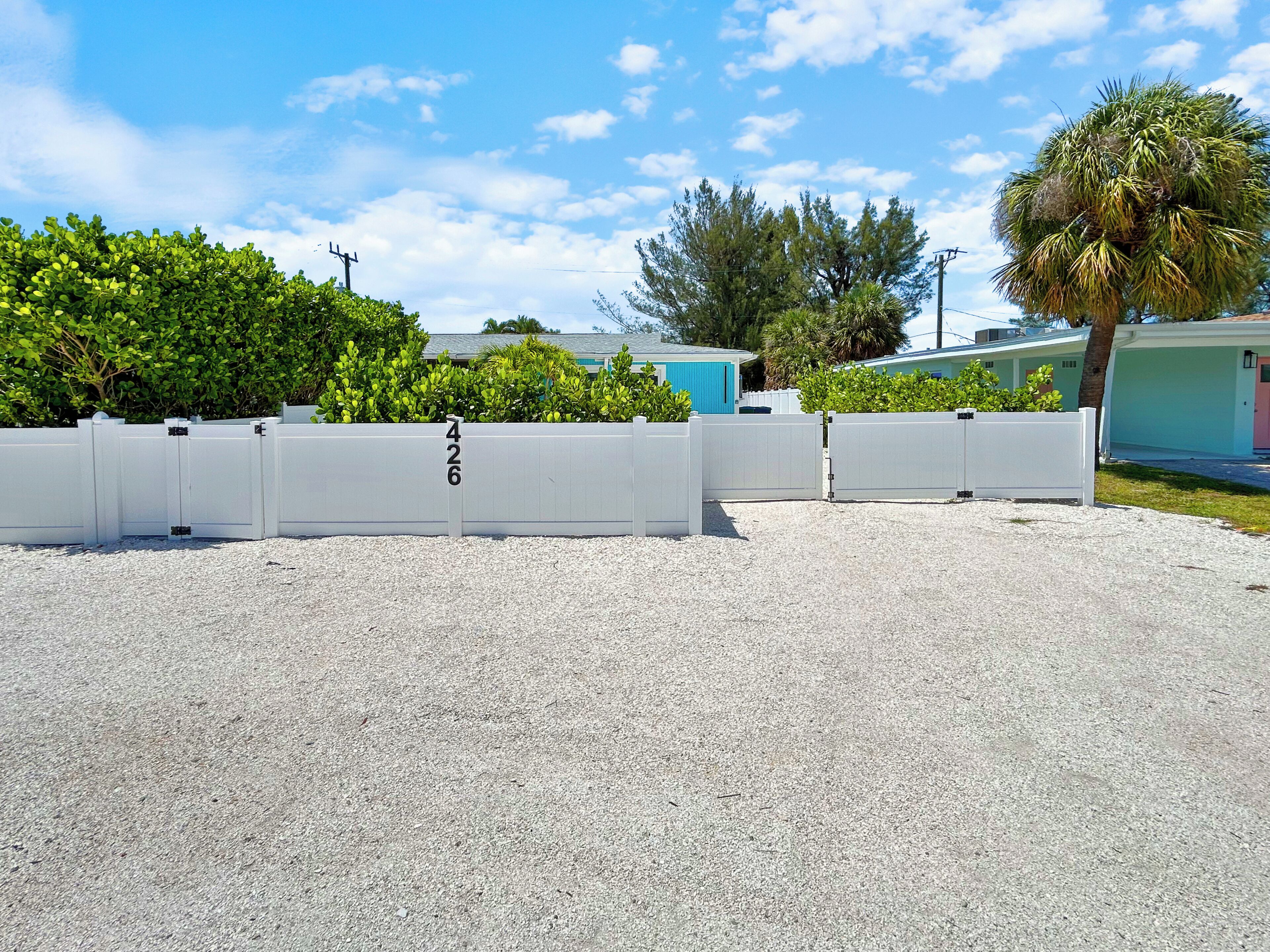 A gated driveway with a number sign, a gravel surface, and a residential building with a blue roof in the background.