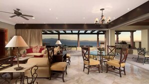 Ein geräumiger Wohnbereich mit hohen Decken, einem Deckenventilator und Bergblick. Es gibt verschiedene Sitzgelegenheiten, darunter eine Couch, Stühle und ein Esstisch.