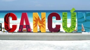 Grandes letras coloridas que deletrean 'CANCÚN' con una playa y el océano al fondo.