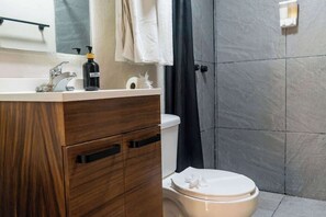 Et badeværelse med en trækommode, et hvidt toilet, en bruseforhæng og en håndklædestang.