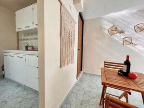 Eine kleine Küche mit weißen Schränken, einem Wandbehang aus Makramee und einem Essbereich mit einem Holztisch und Stühlen.
