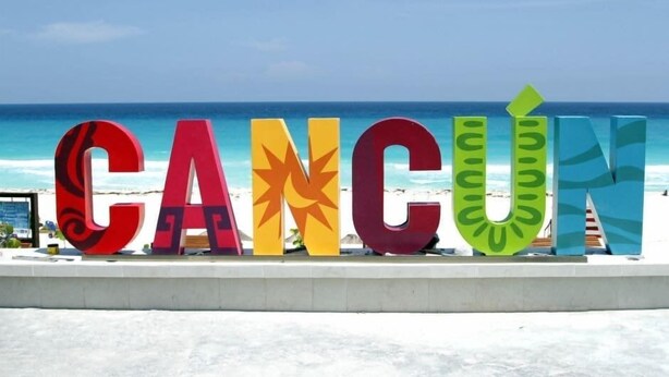 Grandes letras coloridas que deletrean 'CANCÚN' en una playa, con el océano al fondo.