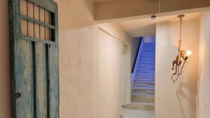 Un pasillo con una escalera, una puerta azul y una lámpara fijada a la pared.