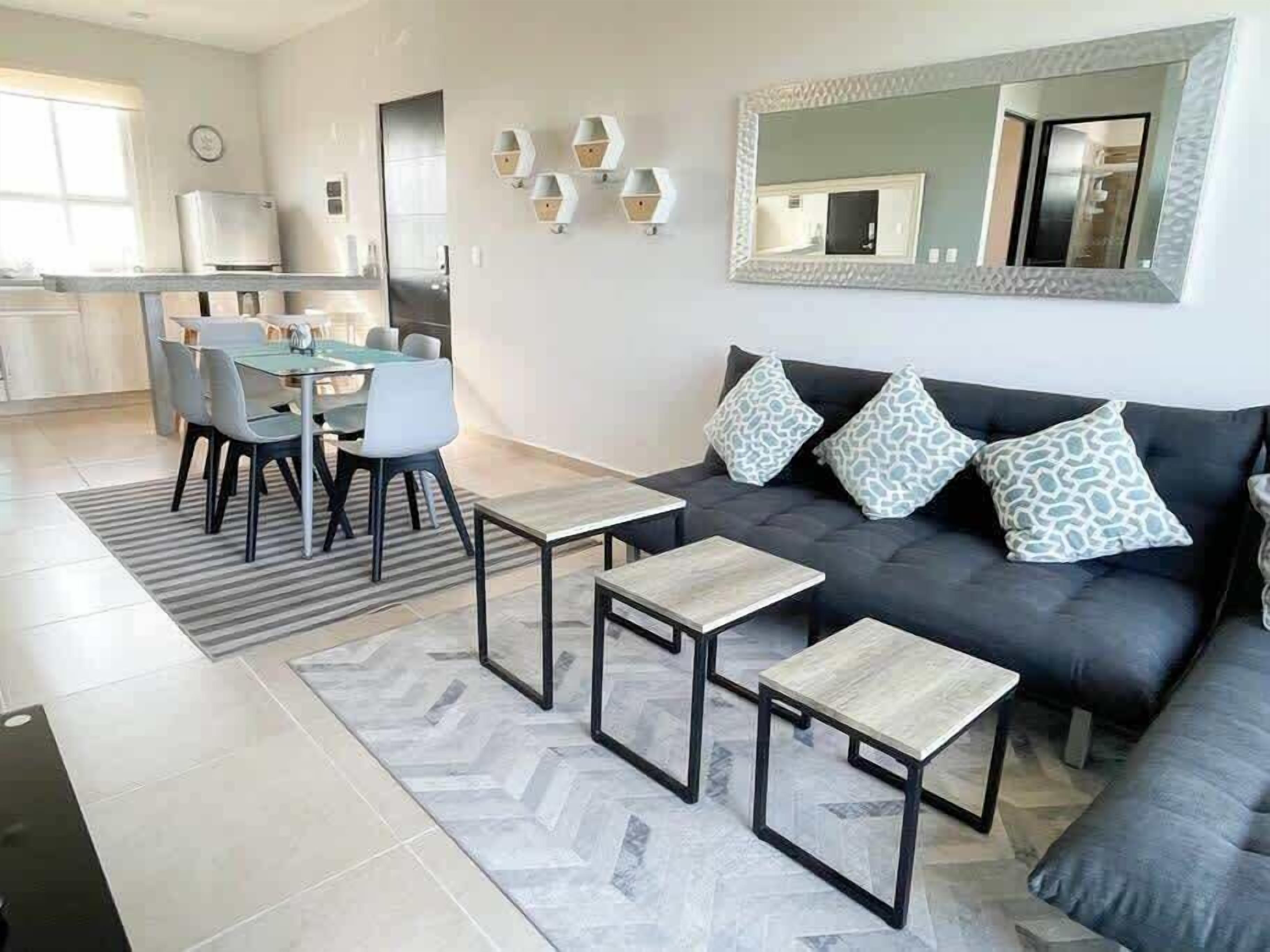 A modern living room with a sofa, two coffee tables, and a dining area with chairs and a table.