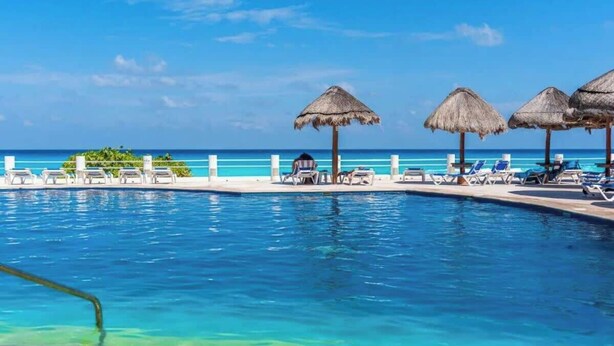 Ein Pool mit klarem, blauem Wasser, Liegestühlen und Strohdächern.