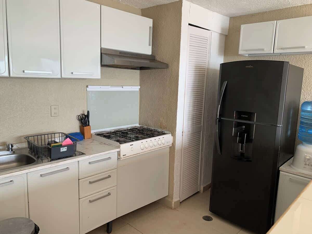 A compact kitchen with white cabinets, a gas stove, a black refrigerator, and a water dispenser.