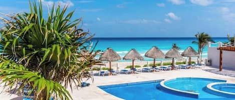 A pool area with lounge chairs and umbrellas, overlooking a beach.