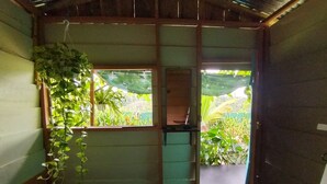 Une pièce avec un lit, une fenêtre donnant sur un espace verdoyant et une porte menant à l’extérieur.