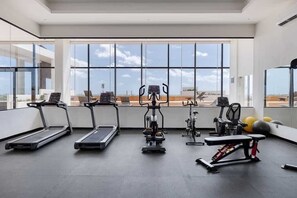 A gym with treadmills, an elliptical, a bench press, and exercise balls, with large windows and a view of the sky. - Cancun 1BR | Lagoon View | Rooftop Pool & Gym (Cancún)