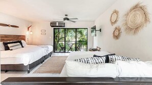 Ein Schlafzimmer mit zwei Betten, einem Deckenventilator, einer Klimaanlage und Blick durch eine Glastür auf einen Außenbereich mit Sitzgelegenheiten.