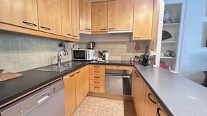 A compact kitchen with wooden cabinets, a black countertop, a dishwasher, a microwave, and a small oven. - Elegant and Peaceful Apartment –  Neuilly-sur-Seine (Neuilly-sur-Seine)
