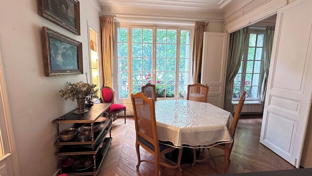 Zona pranzo con tavolo, sedie, credenza e una grande finestra con tende.