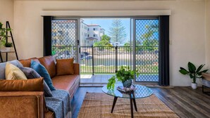 A living room with a leather sofa, a glass coffee table, and a view of a residential area through large sliding glass doors. - Canal Luxury living & boat ramp (Runaway Bay)