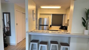 A compact kitchen with a central island, four stools, a refrigerator, and a microwave. - 2-bedroom apartment in Waikiki with PARKING included (Honolulu)